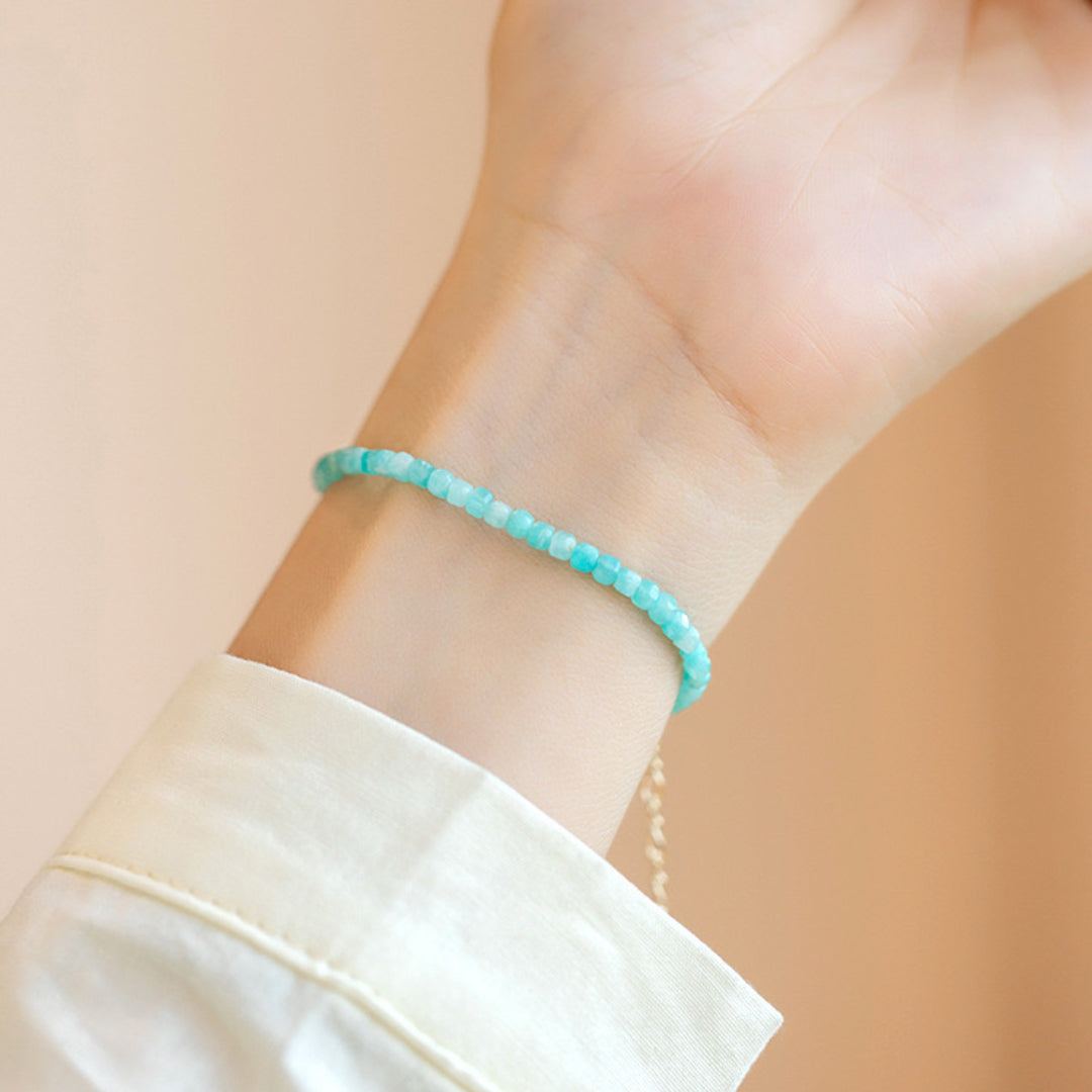 Bracelet fin en amazonite bleu clair sur un poignet, avec une chemise blanche et un fermoir doré.