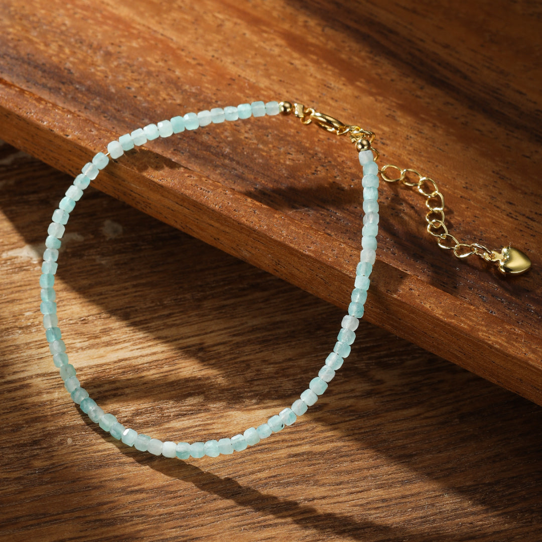 Bracelet Fil d'Azur en amazonite fine avec fermoir doré et pendentif cœur, posé sur un fond en bois.