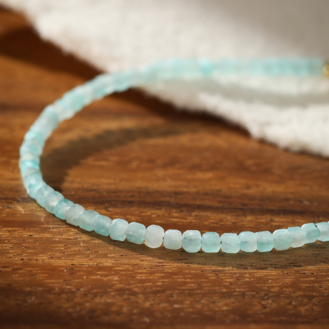 Bracelet fin en amazonite naturelle aux perles facettées bleu pâle, sur fond de bois.