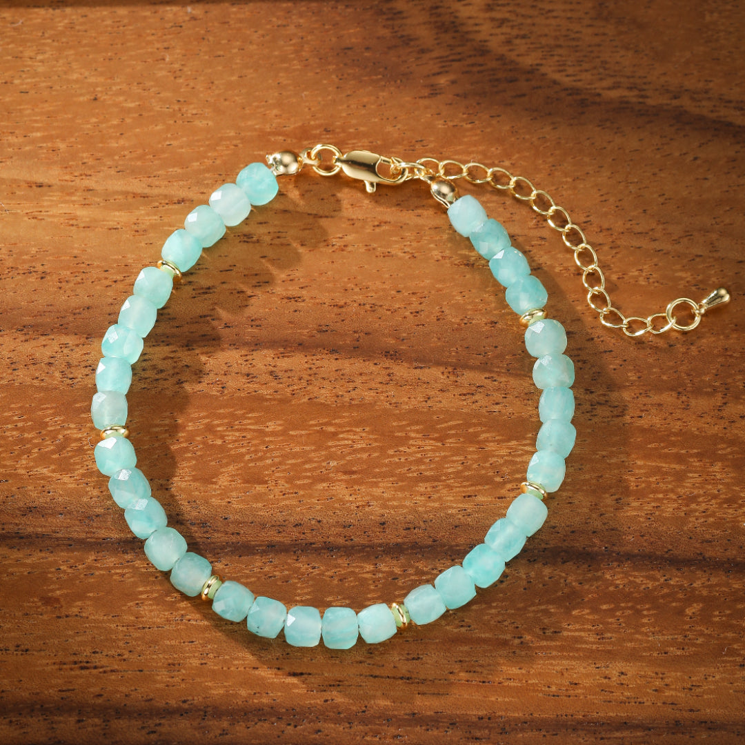 Bracelet en amazonite bleue avec des petites perles dorées et une chaîne d'extension, posé sur un fond en bois.