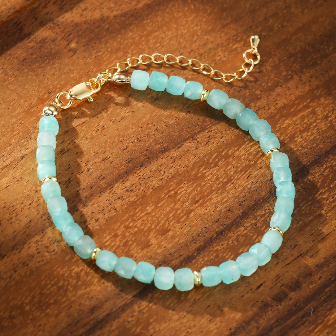 Bracelet fait de petites perles cubiques d'amazonite bleu-vert pâle, séparées par de petites perles rondes dorées, avec une chaîne d'extension dorée et un fermoir mousqueton.