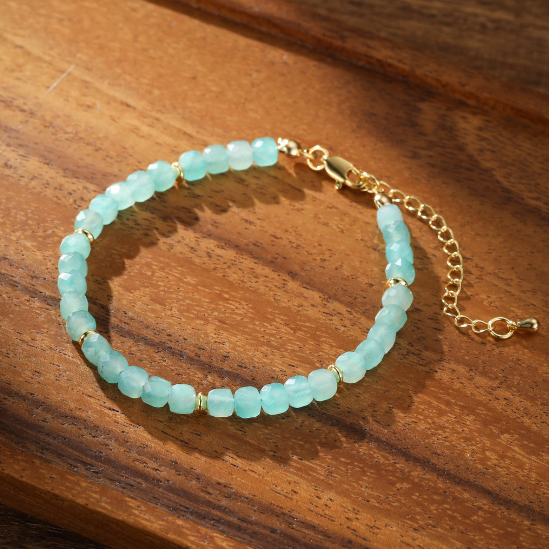 Bracelet en amazonite naturelle avec des perles facettées bleu-vert pâle et des accents dorés, sur un fond en bois.