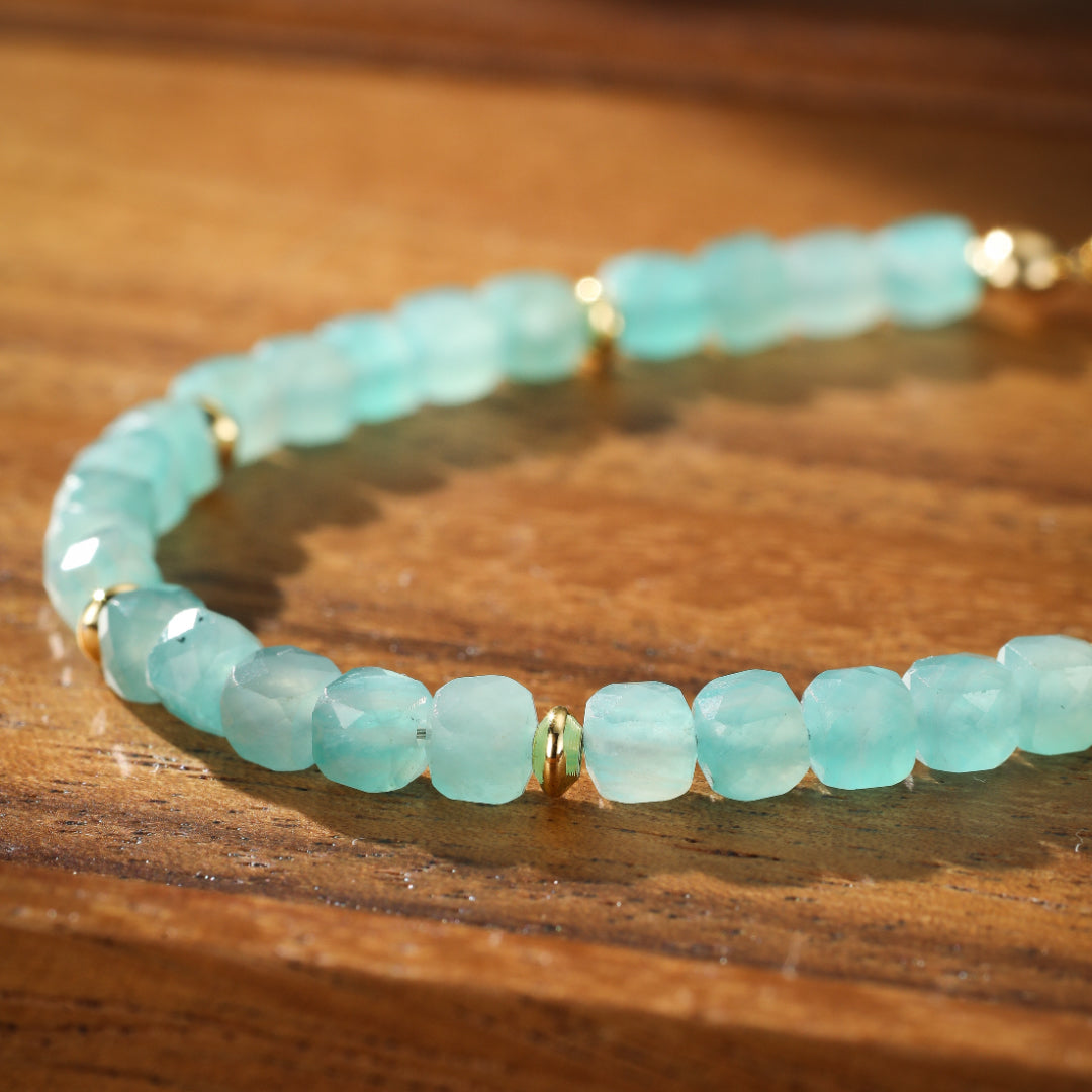 Bracelet en amazonite aux perles facettées bleu pâle et discrets intercalaires dorés, sur fond de bois naturel.