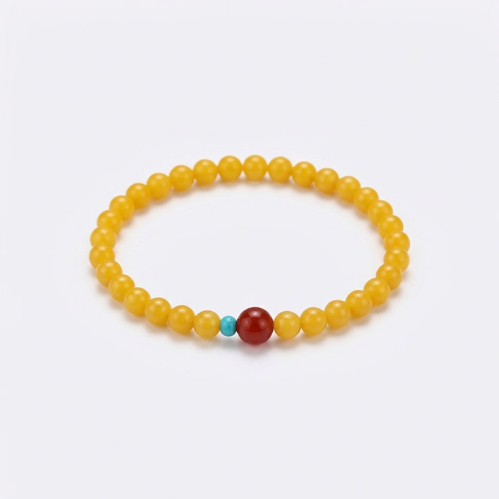 Bracelet artisanal Mémoire de la Terre composé de perles d'ambre jaune avec une perle centrale en agate rouge et une petite perle en turquoise sur fond blanc.