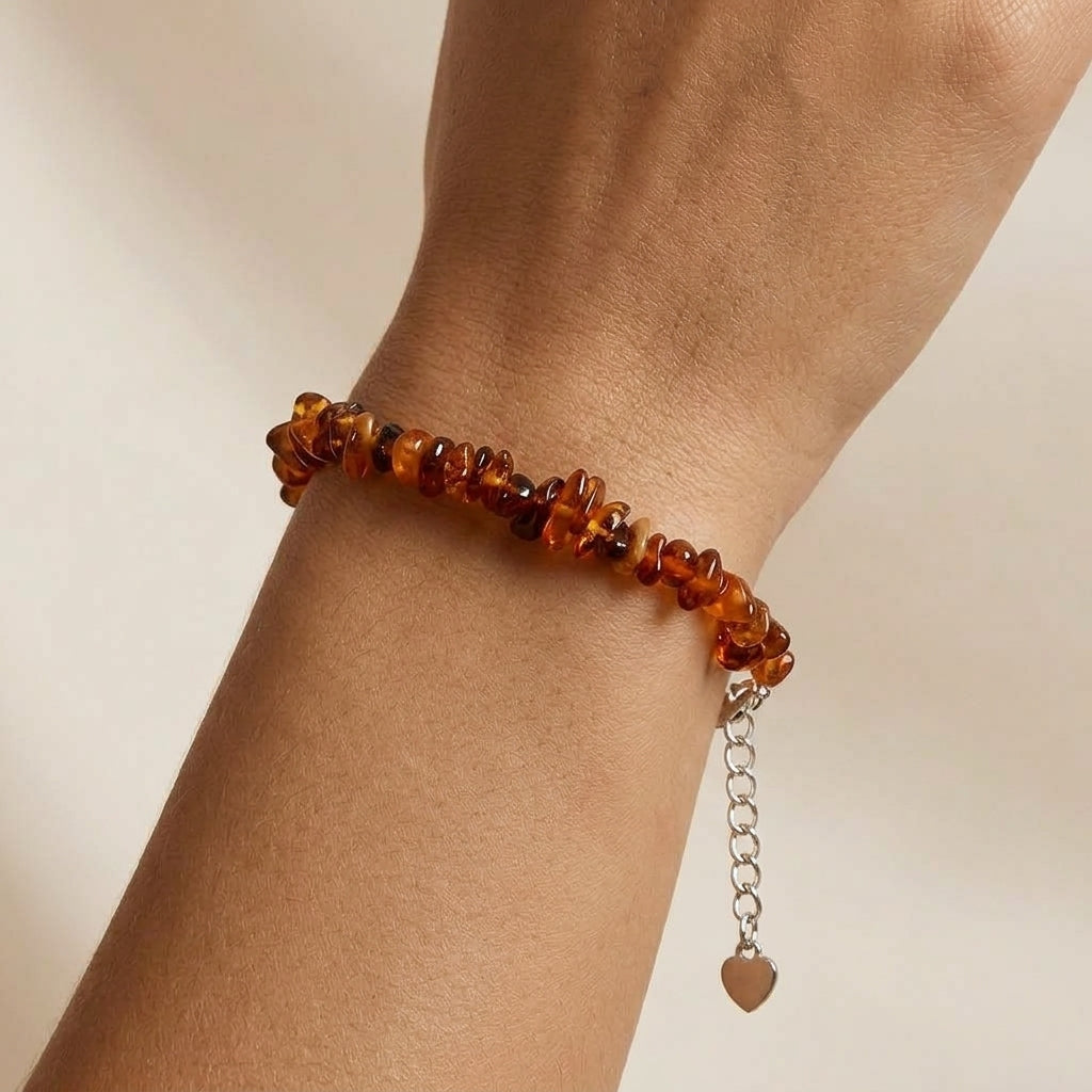Bracelet en ambre naturel Soleil Éternel composé de petites perles brutes aux tons chauds porté au poignet avec une chaînette de réglage en argent et un petit pendentif cœur.