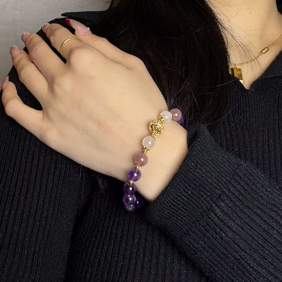Gros plan sur un bracelet en pierres naturelles d'améthyste et de quartz fraise, porté au poignet d'une femme avec un pull noir et une bague dorée.