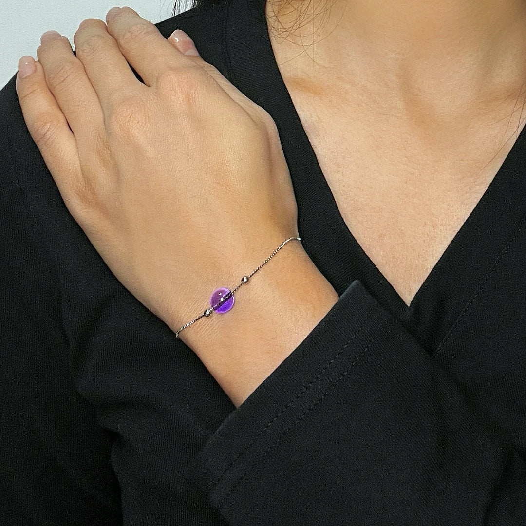 Bracelet en argent avec une perle d'améthyste ronde et lisse, ornée de petites perles argentées, portée au poignet d'une femme.