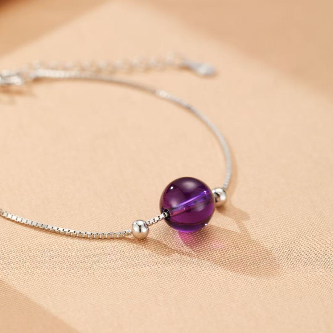 Bracelet en argent avec une perle d'améthyste ronde et deux petites perles argentées, sur fond beige.