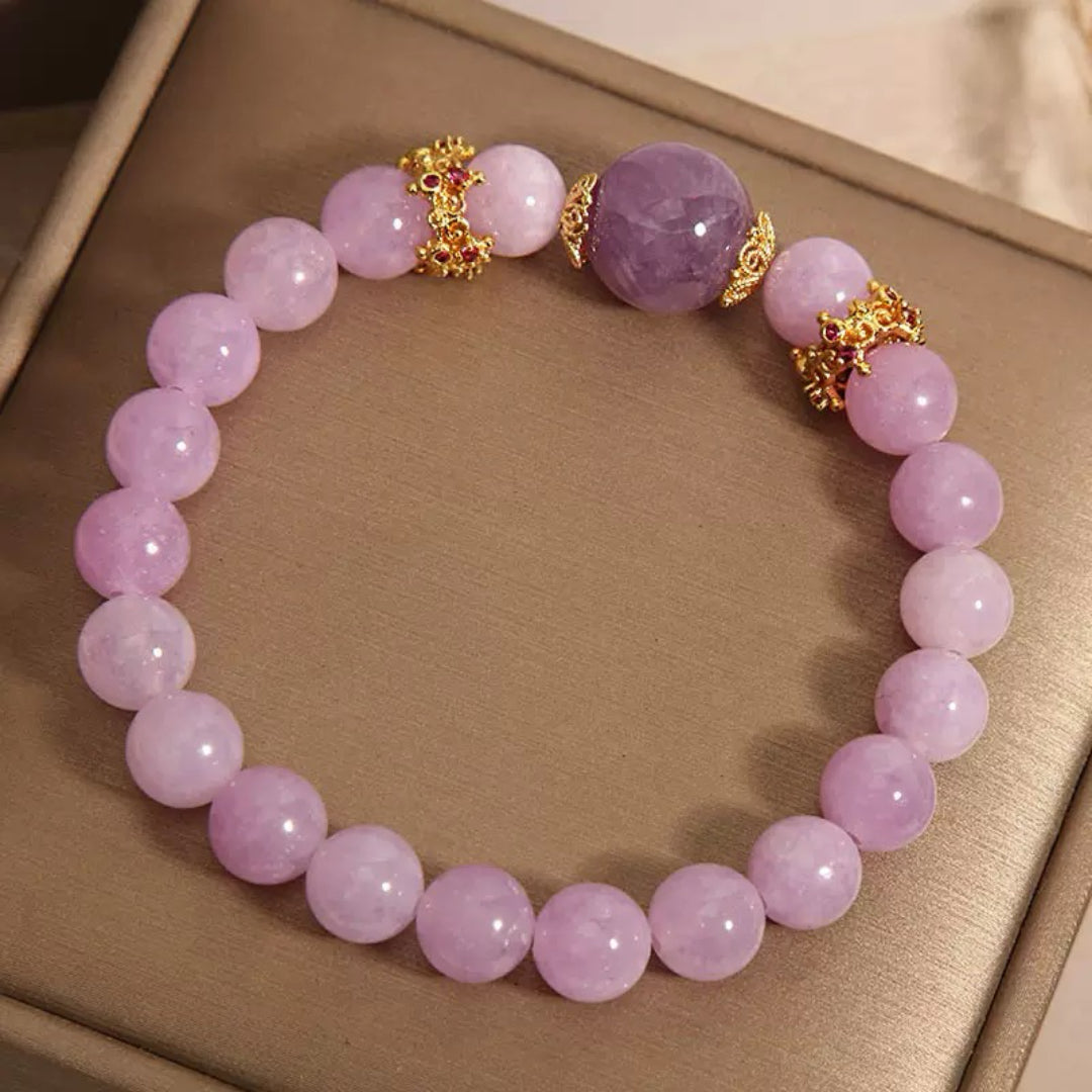 Bracelet en perles lavande clair et une grosse perle d'améthyste centrale, orné de fermoirs dorés et de pierres rouges.
