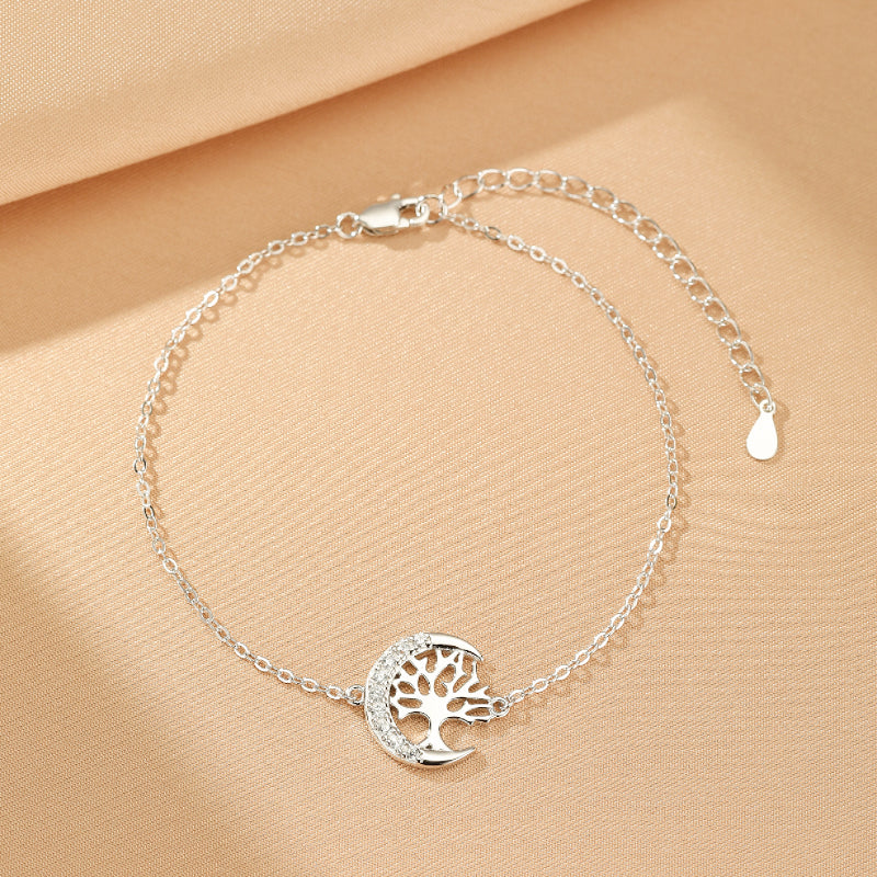 Bracelet Arbre de Vie en argent avec un pendentif en forme de croissant de lune orné d'un arbre stylisé et de petites pierres scintillantes.