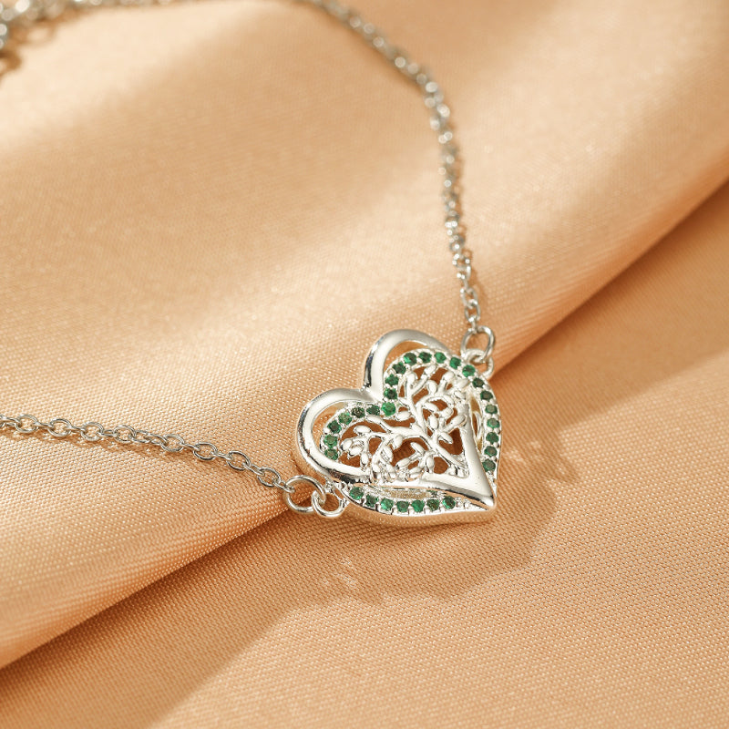 Bracelet Arbre de Vie en argent avec un cœur ajouré serti de zircons verts sur un fond satiné.