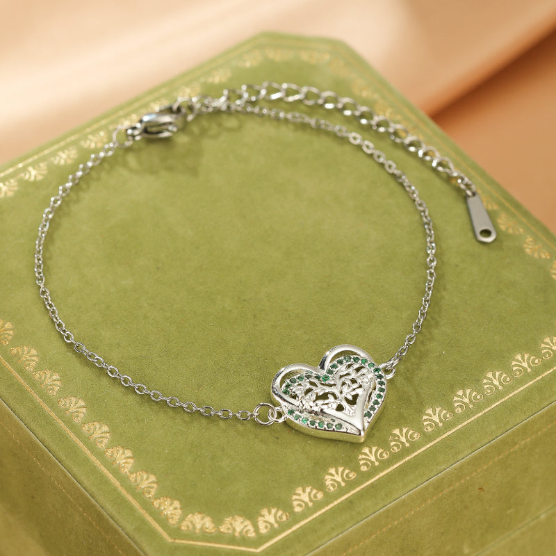 Bracelet en argent avec un pendentif en forme de cœur ajouré orné d'un arbre de vie et de petites pierres vertes.