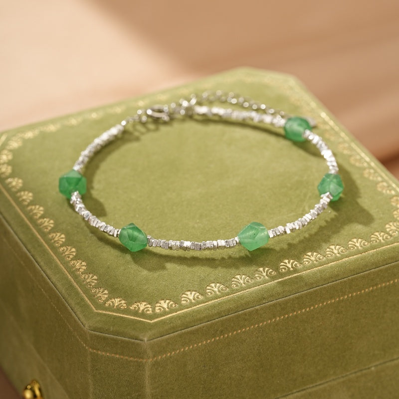 Bracelet en argent orné de perles d'aventurine verte taillées en forme de cube et de petites perles argentées, posé sur une boîte à bijoux verte.