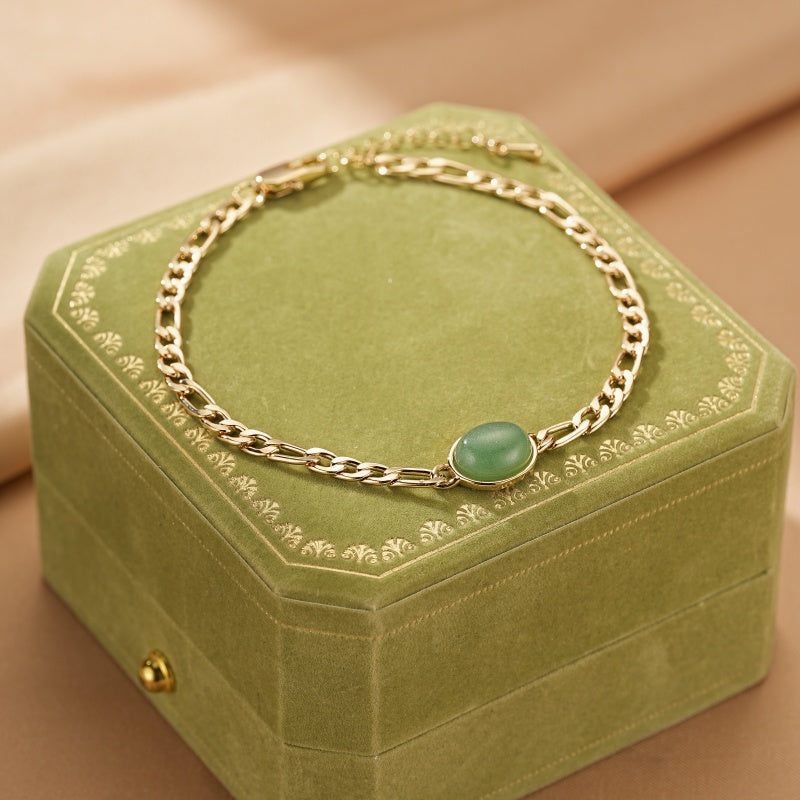 Bracelet en plaqué or avec une pierre d'aventurine verte ovale sur une boîte à bijoux verte.