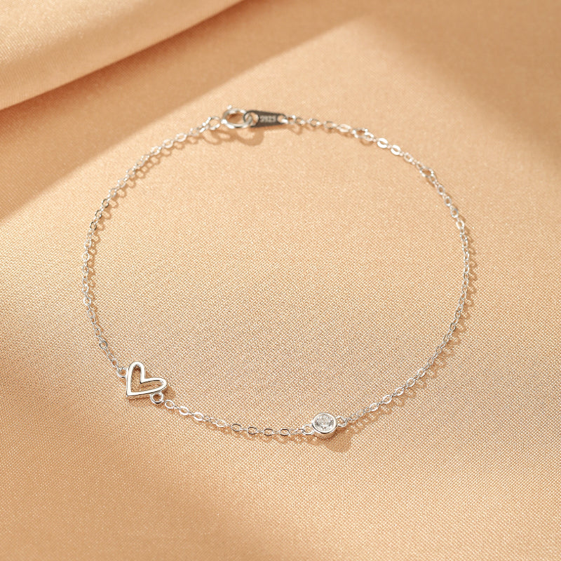 Bracelet fin en argent avec un pendentif cœur ajouré et une petite pierre transparente sertie sur une chaîne délicate.