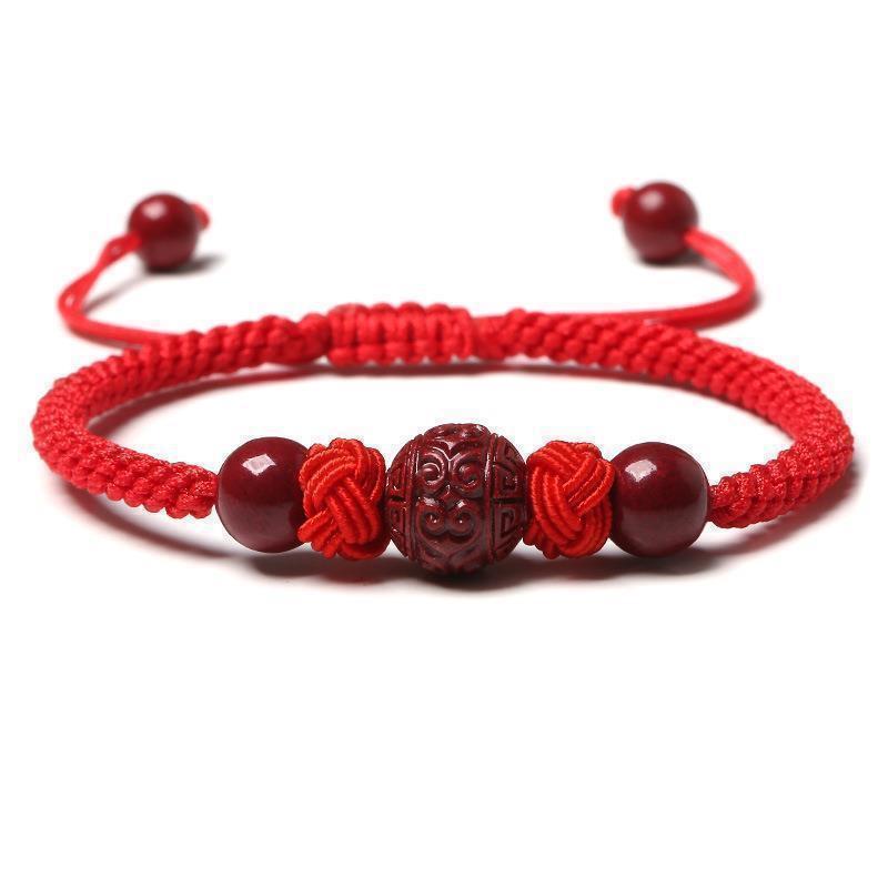 Bracelet tressé rouge avec des perles en cinabre sculptées et lisses, symbolisant la chance et le bonheur.