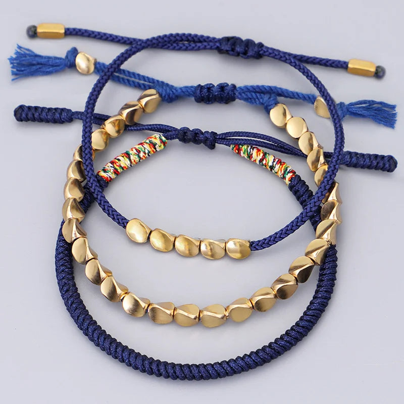 Trois bracelets en cordon bleu marine ornés de perles dorées texturées et d'un fil multicolore, fermoir réglable avec pompons.