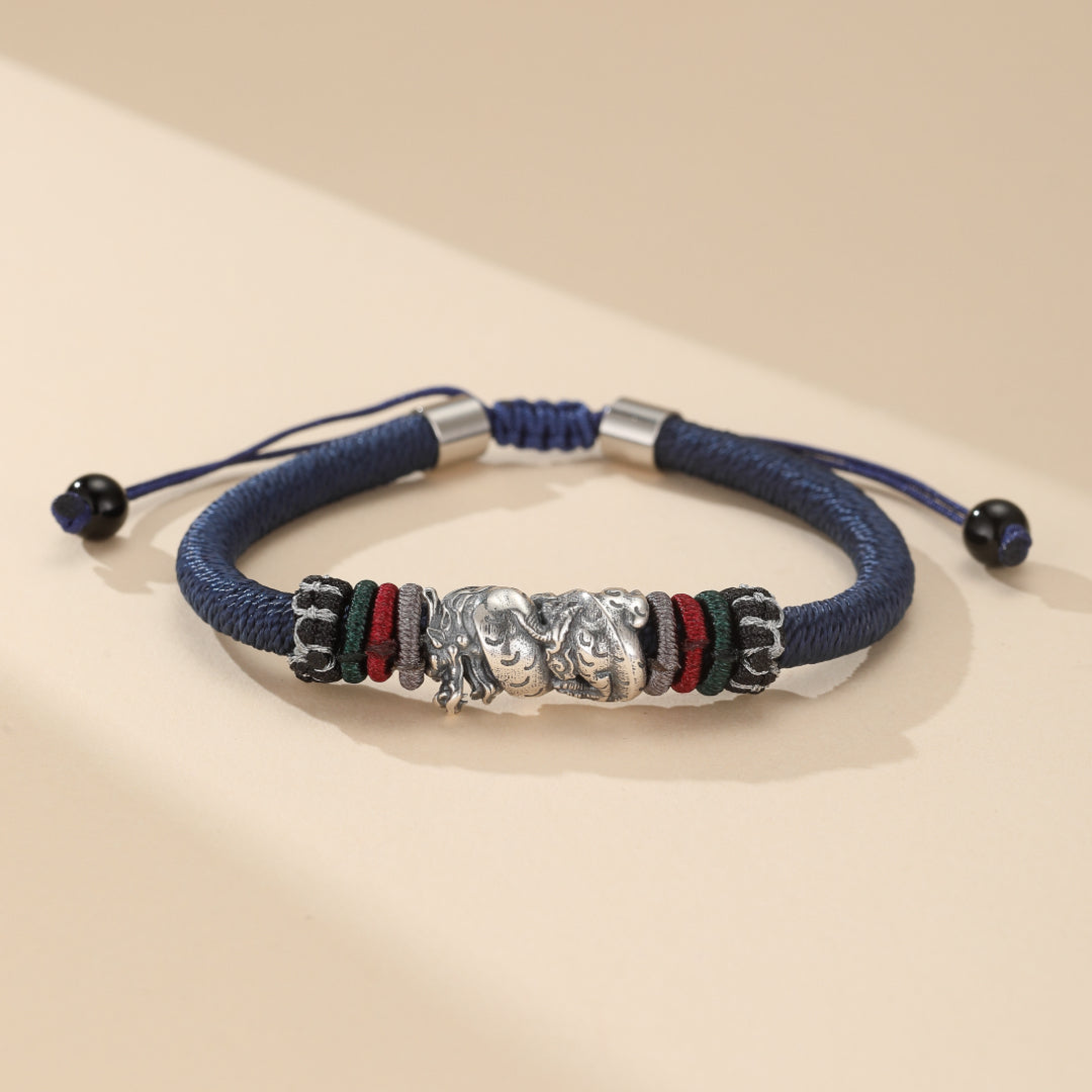 Bracelet cordon bleu orné d'un motif de dragon en argent et de fils colorés vert, rouge et noir.