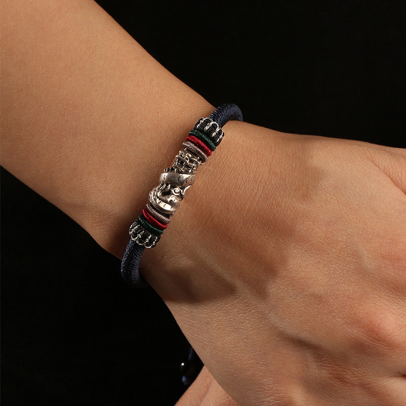 Bracelet cordon esprit du dragon en argent avec détails de fils tibétains rouges, verts et noirs sur un poignet.