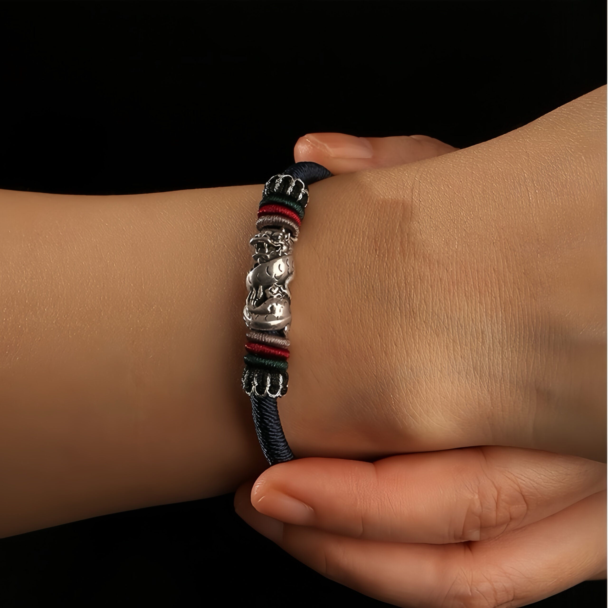 Bracelet cordon avec un dragon en argent et des fils colorés rouges, verts et noirs, porté au poignet.