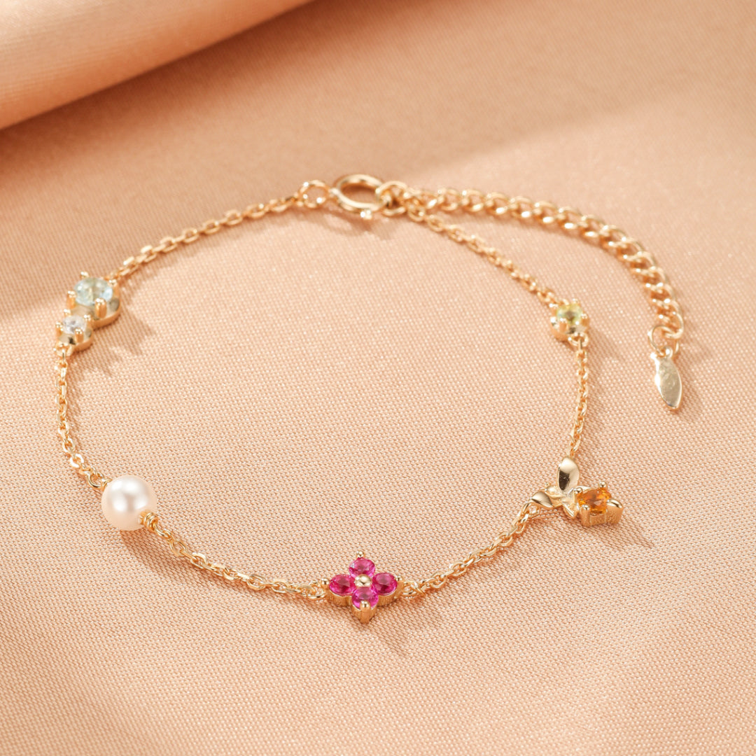 Bracelet "Jardin Enchanté" en argent doré, orné d'une perle, d'une fleur rose, d'un papillon orange et de petites pierres bleues et vertes.