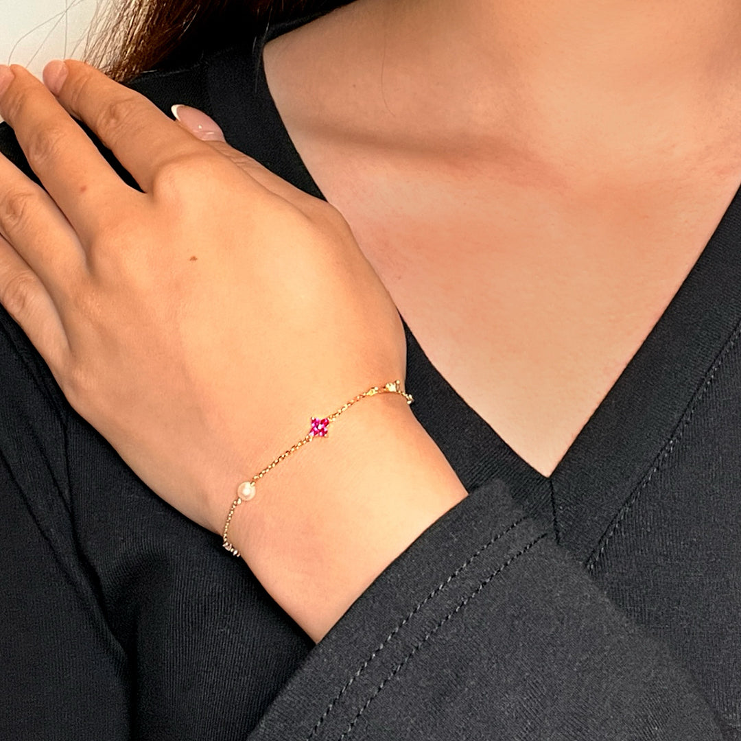 Bracelet fin en argent avec une pierre rose en forme de fleur et une perle, porté au poignet.