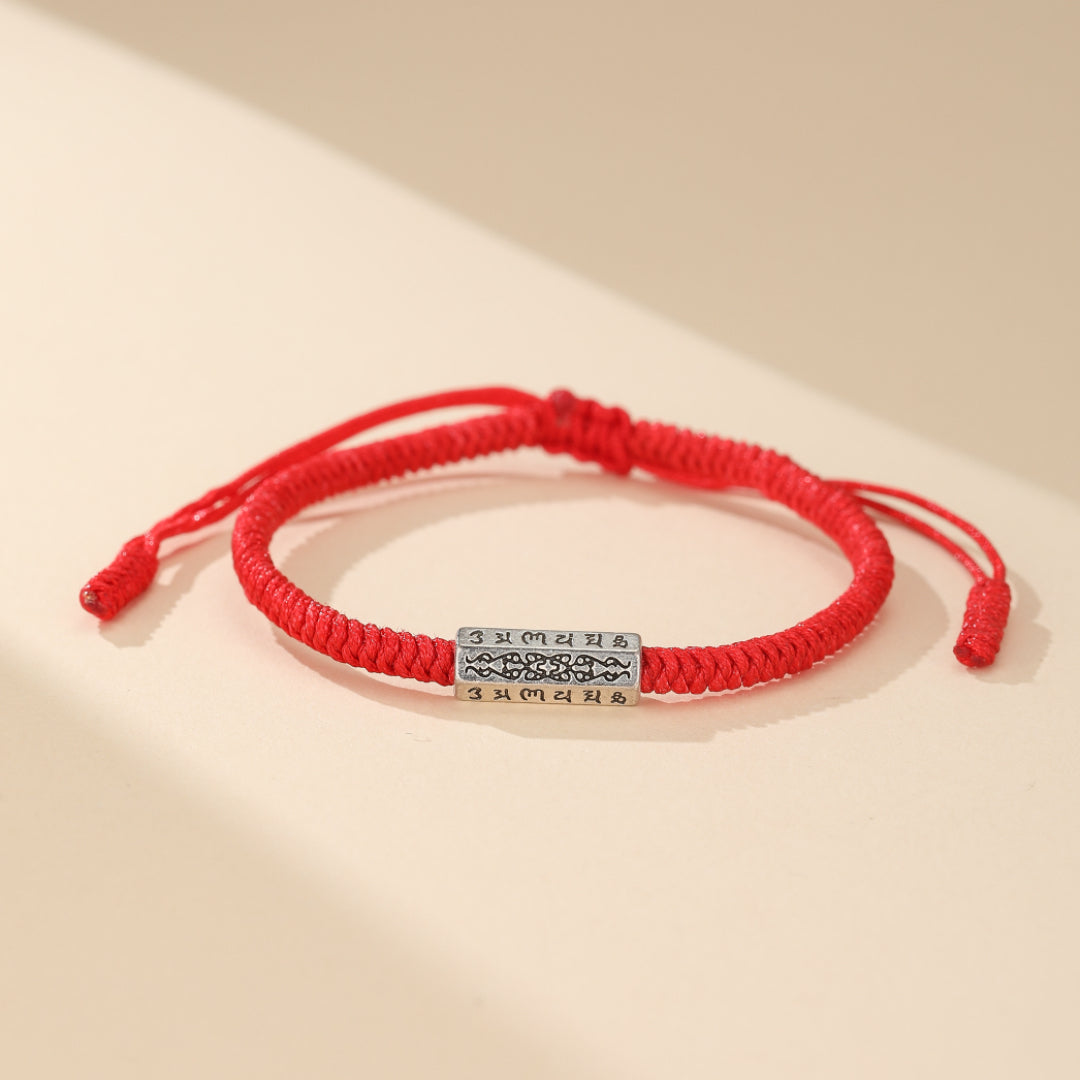 Gros plan sur la perle finement gravée de mantras tibétains du bracelet 'Mantras' en fil rouge, fait main pour la chance et la paix intérieure.