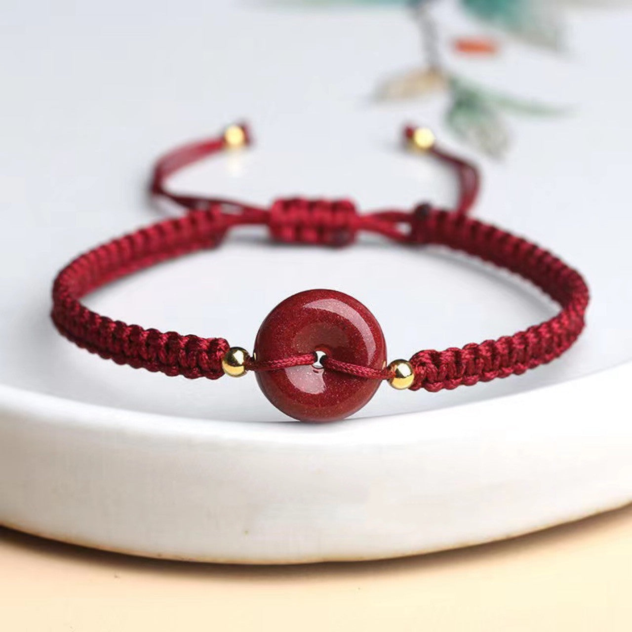 Bracelet cordon réglable rouge avec une perle centrale ronde rouge et des petites perles dorées de chaque côté.