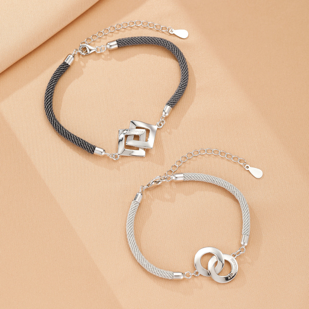 Deux bracelets assortis pour couple : un bracelet en cordon gris avec un pendentif carré entrelacé en argent et un bracelet en cordon argenté avec deux anneaux entrelacés en argent, symbolisant l'union.