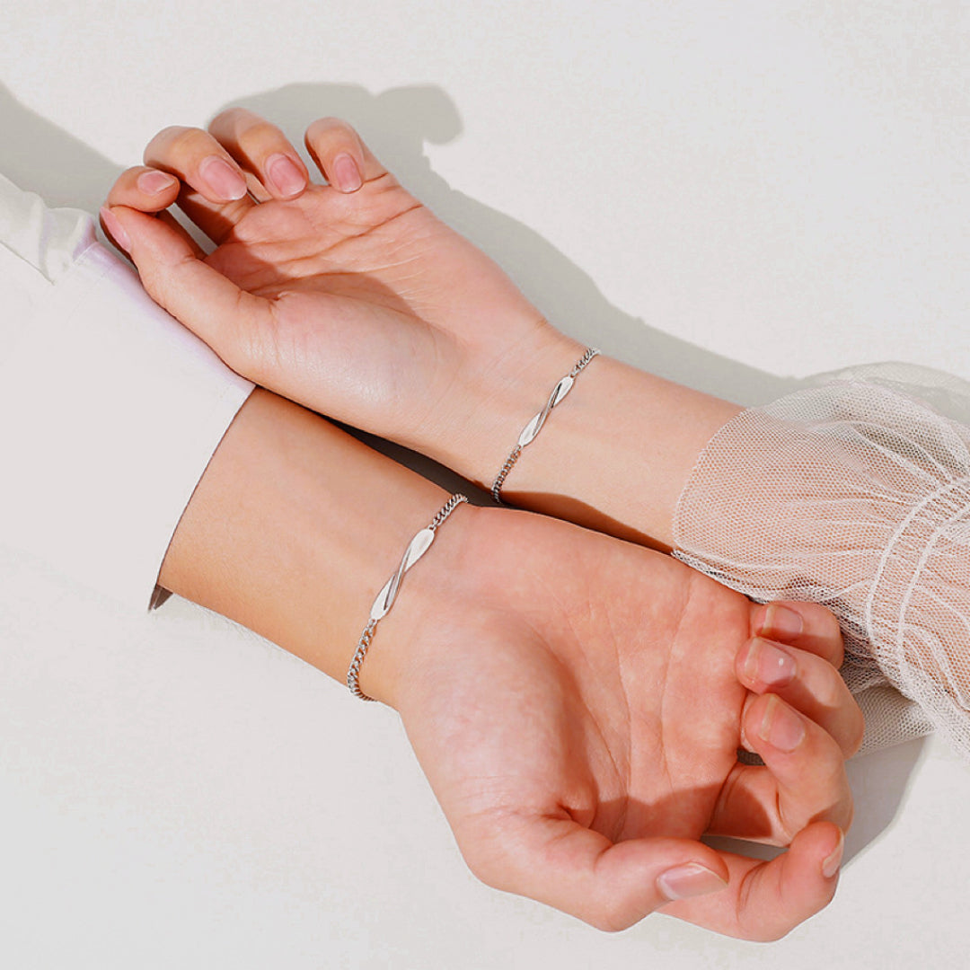 Deux bracelets fins en argent reliés par un lien symbolique, portés par un couple.