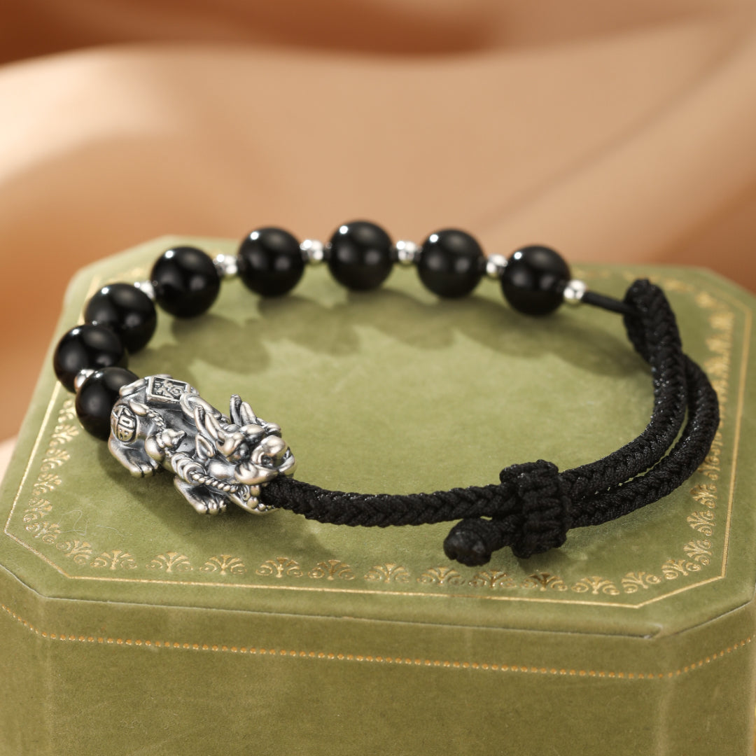 Bracelet Pi Xiu en argent avec perles noires et fil rouge, orné d'une créature mythique chinoise.