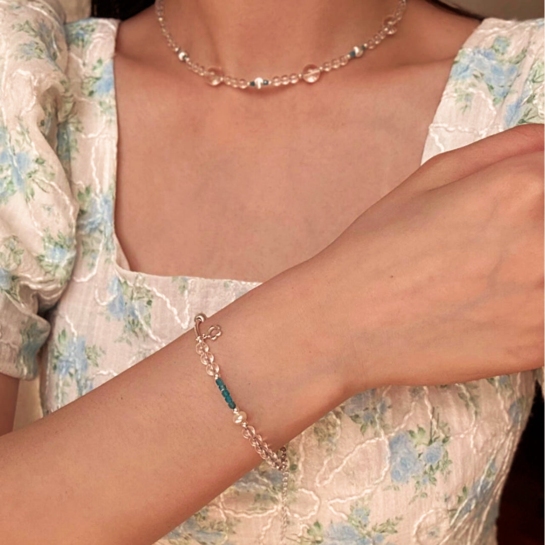 Bracelet "Onde Joyeuse" en argent avec des pierres de cristal de roche et d'apatite bleues sur le bras d'une femme portant une robe fleurie.