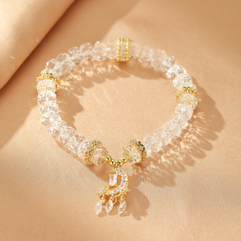 Bracelet en cristal de roche avec un pendentif en forme de croissant de lune orné de zircons et de gouttes de cristal pendantes, monté sur un cordon élastique avec des perles dorées.