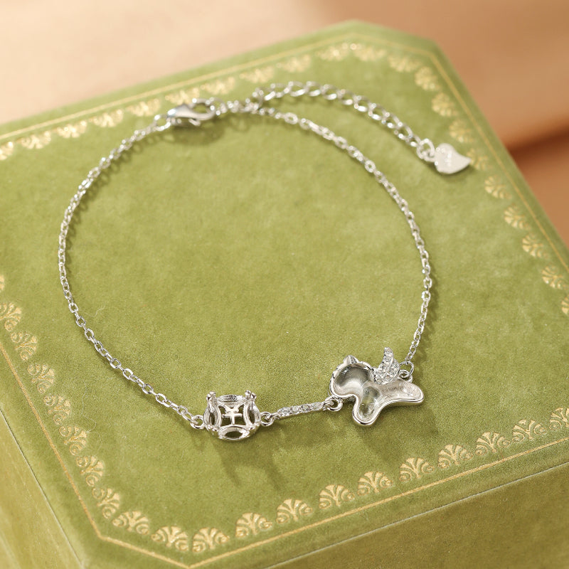 Bracelet en argent avec un cristal de roche carré et un pendentif en forme d'animal ailé orné de petites pierres scintillantes, posé sur un écrin vert.