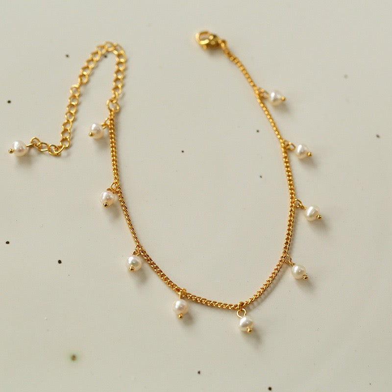 Bracelet de cheville plaqué or avec de petites perles blanches suspendues à une fine chaîne.