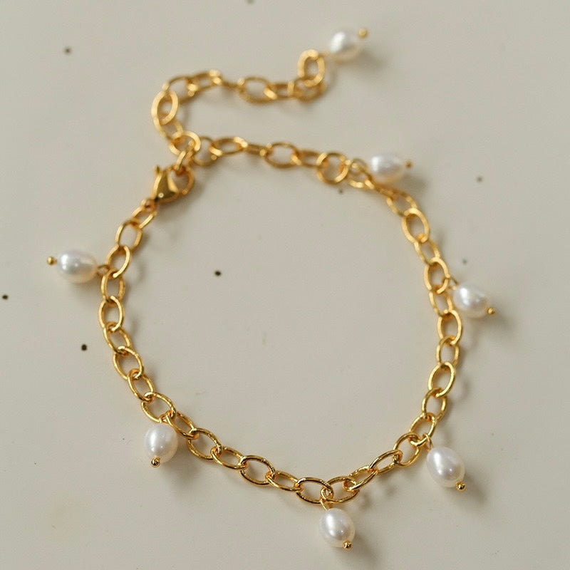 Bracelet de cheville plaqué or avec de petites perles blanches suspendues à une chaîne.