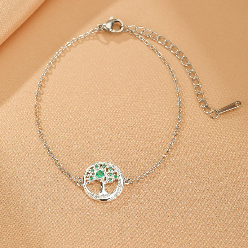 Bracelet en argent fin avec un pendentif rond orné d'un arbre de vie stylisé avec des feuilles d'émeraude et des détails scintillants.