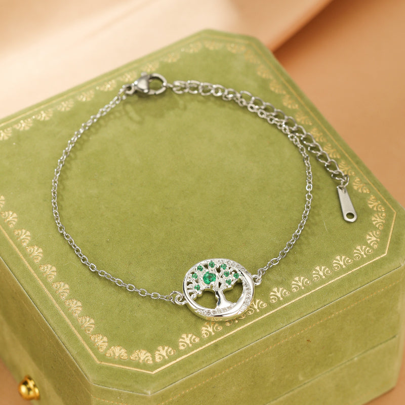 Bracelet en argent avec un pendentif arbre de vie serti d'émeraudes et de diamants, sur fond vert.