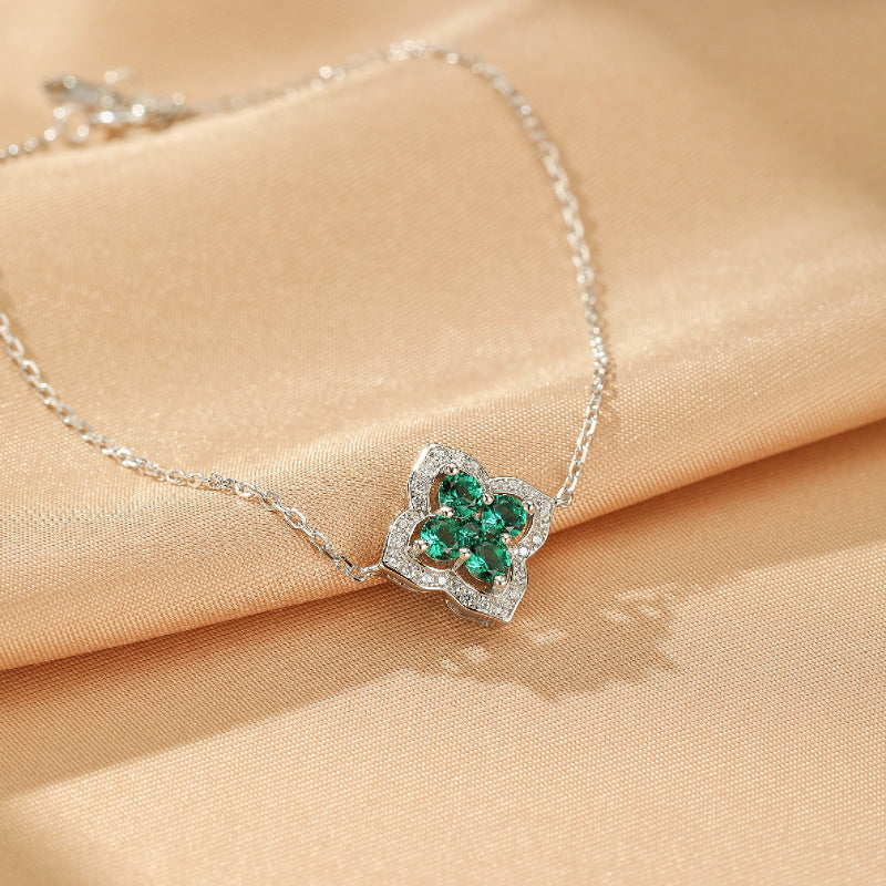 Bracelet en argent 925 avec un pendentif en forme de fleur de trèfle orné de pierres d'émeraude et de cristaux scintillants, posé sur un tissu satiné couleur pêche.