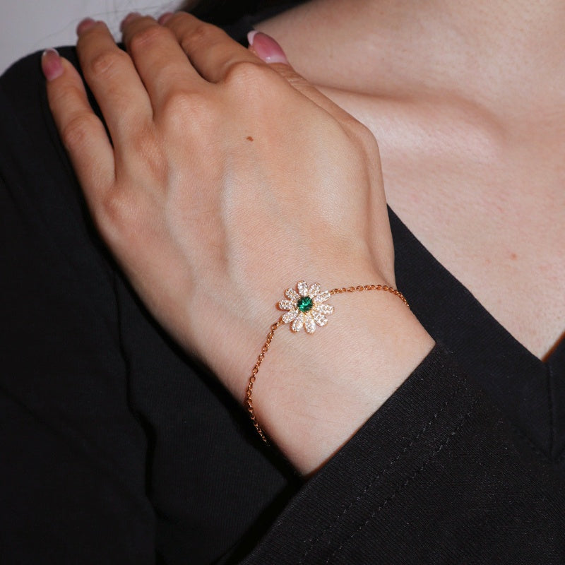 Bracelet en argent plaqué or 18K avec un motif de fleur sertie d'une émeraude centrale et de zircons scintillants, porté au poignet d'une femme.