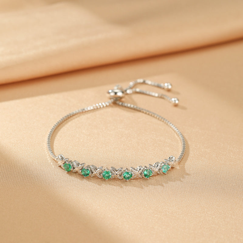 Bracelet en argent avec des zircons verts disposés en forme de X sur une chaîne réglable.