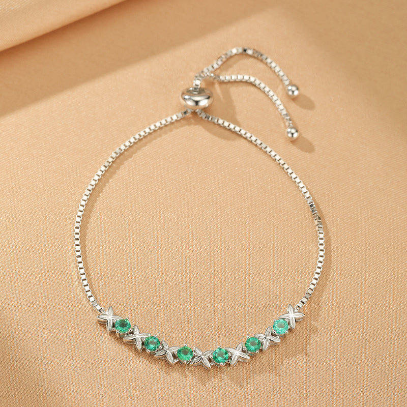 Bracelet en argent avec des motifs floraux et des pierres d'émeraude rondes serties, sur un fond beige satiné.