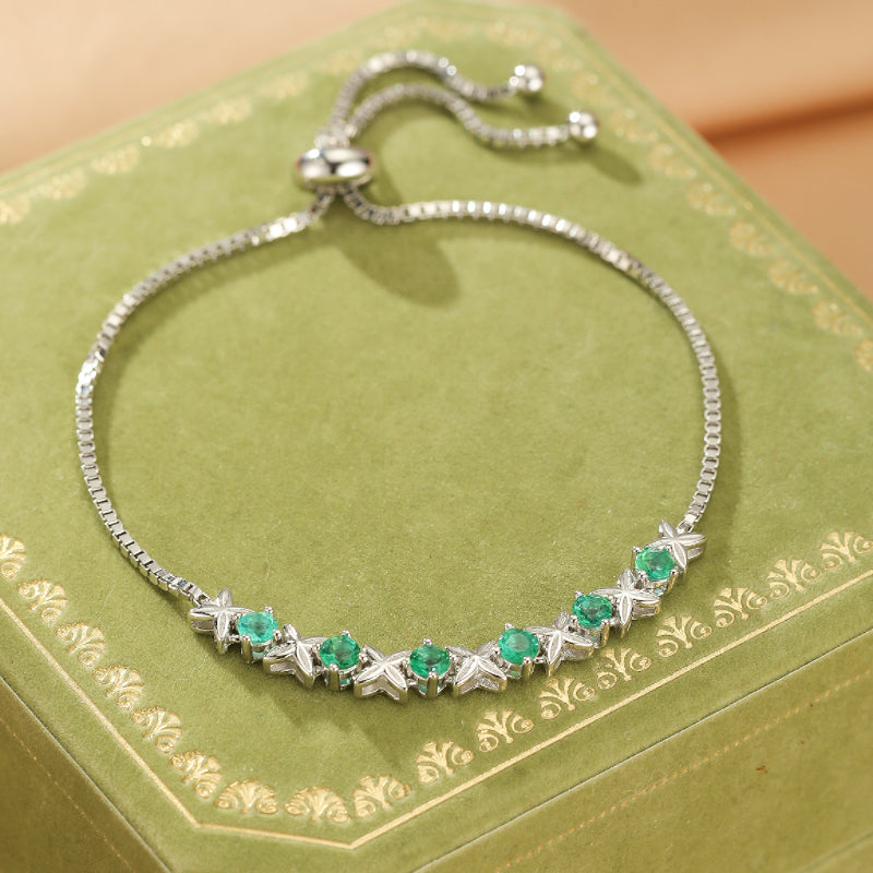 Bracelet en argent avec des émeraudes rondes et des étoiles serties, ajustable, sur un fond vert orné.