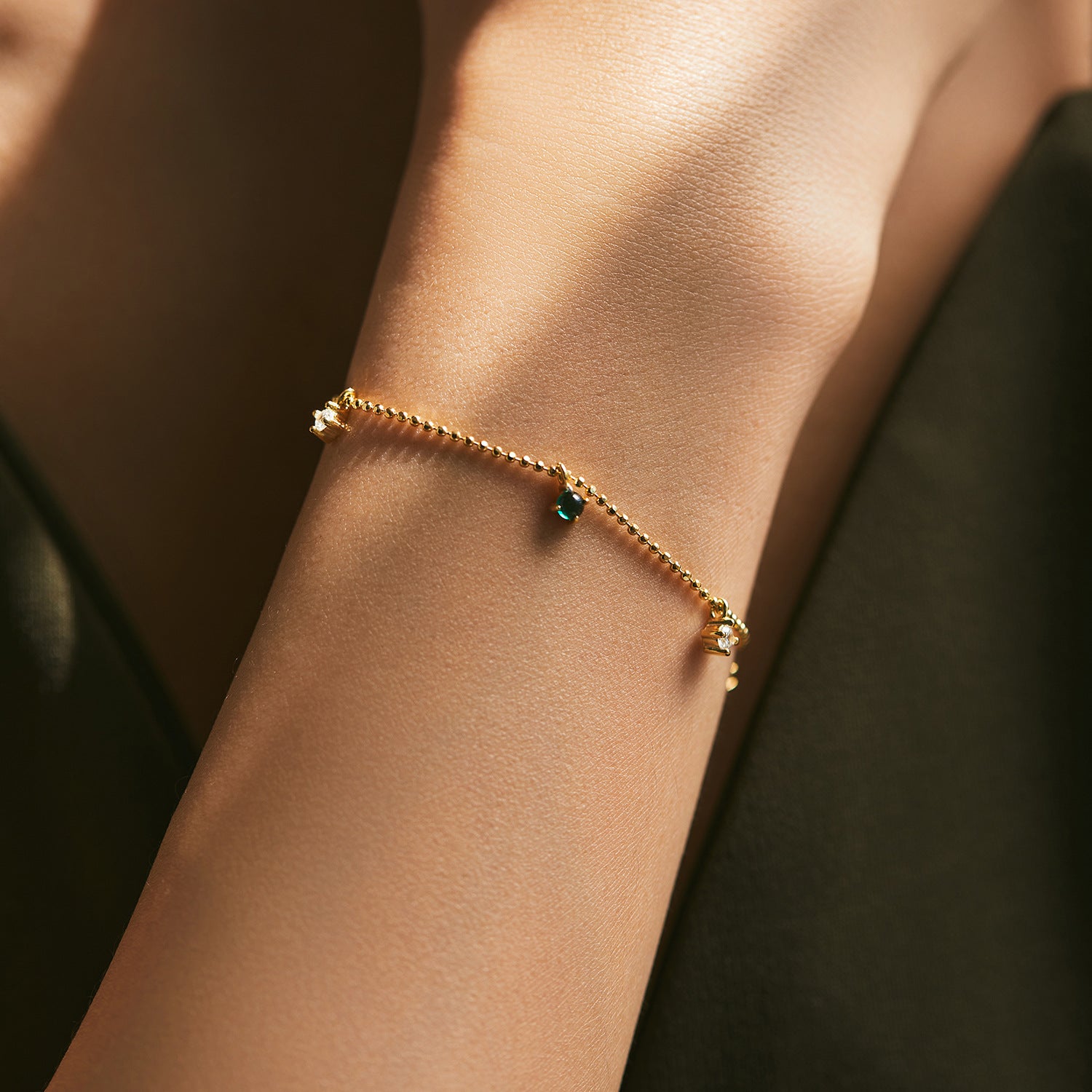 Bracelet en argent 925 plaqué or avec une petite émeraude verte et deux petites pierres blanches, porté au poignet d'une femme.