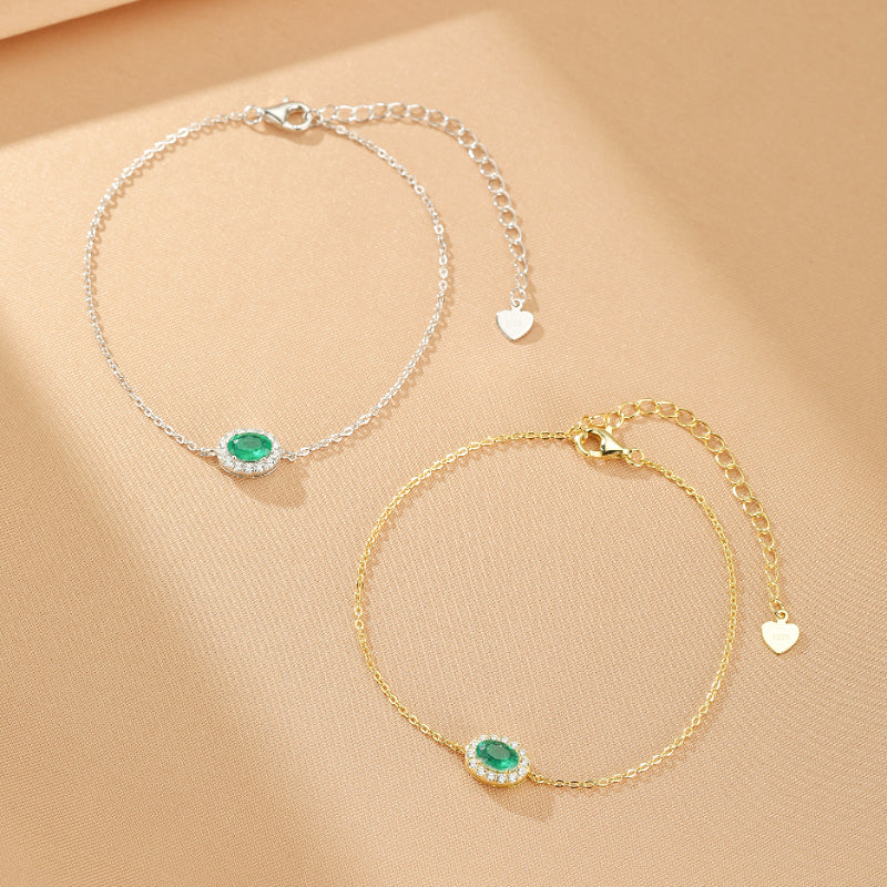 Deux bracelets délicats, l'un en argent plaqué or et l'autre en argent, ornés chacun d'une émeraude ovale entourée de petites pierres scintillantes.
