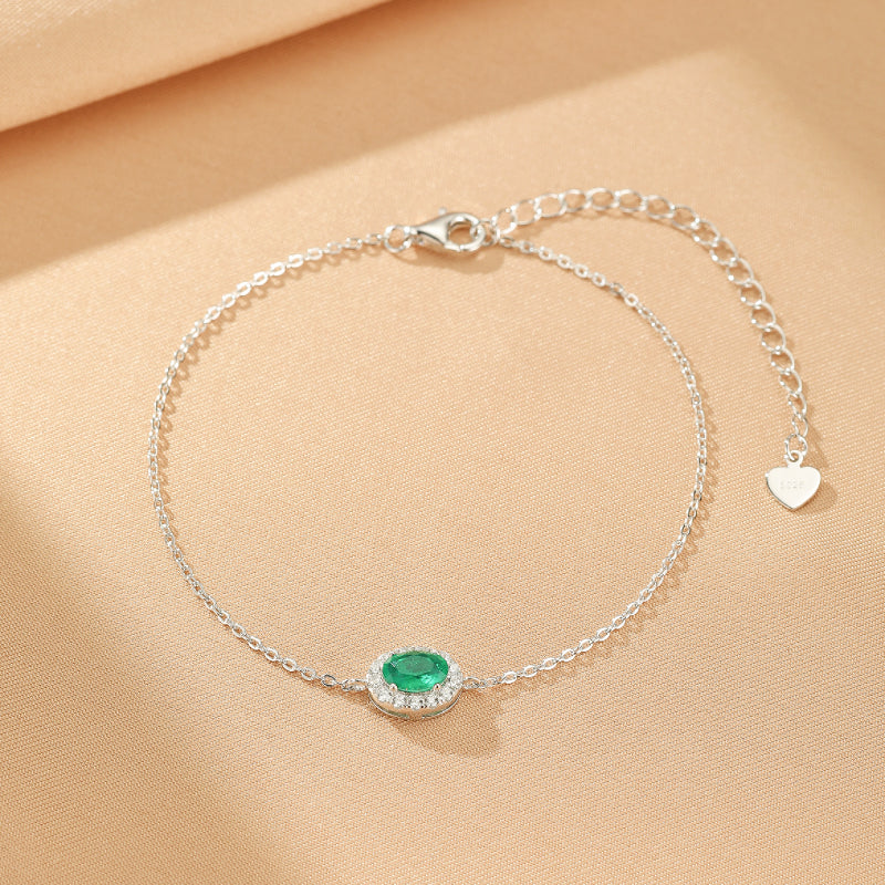 Bracelet en argent plaqué or avec une émeraude ovale entourée de petits cristaux, fermoir mousqueton et pendentif cœur.