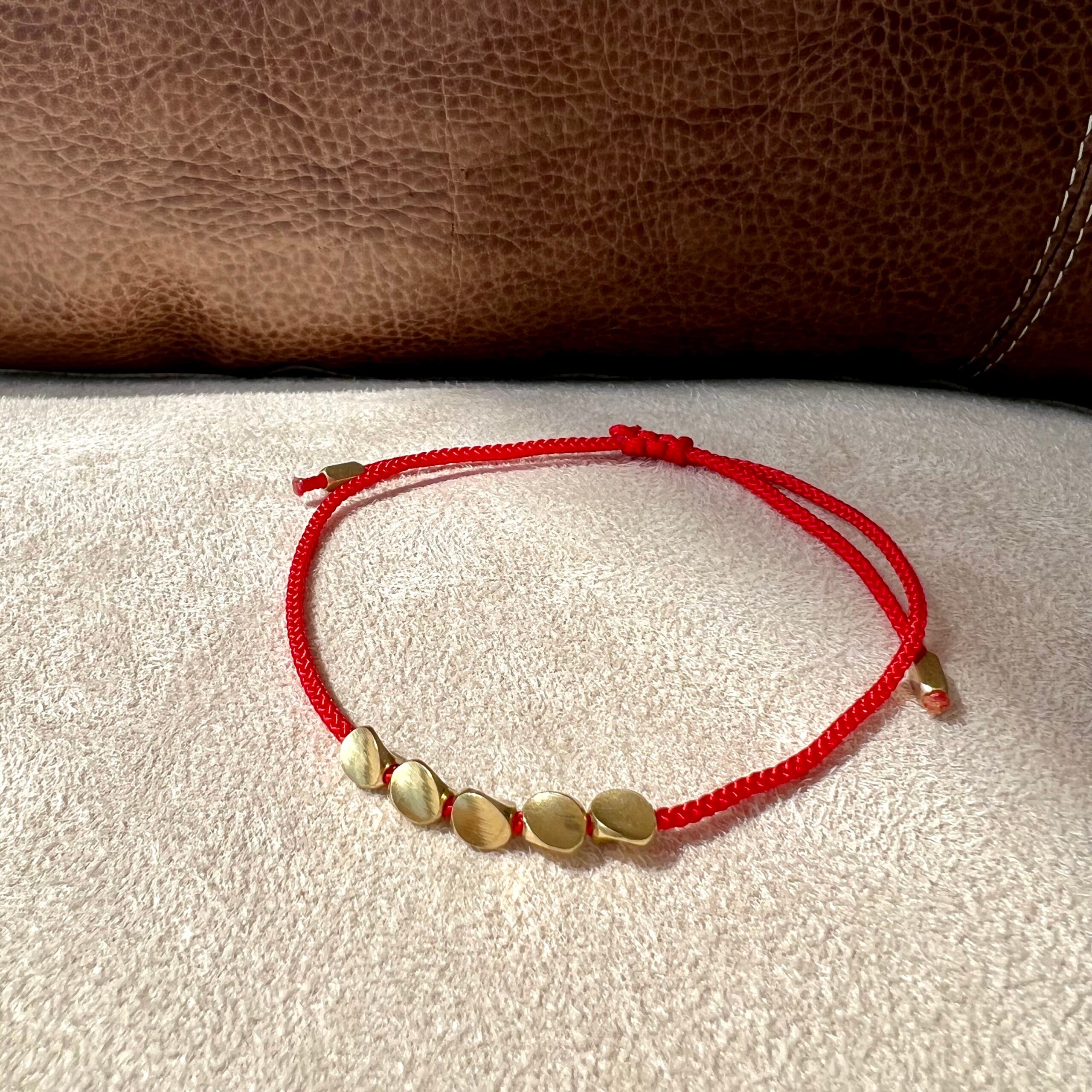 Bracelet fil rouge avec cinq petites perles dorées plates, fermoir réglable.