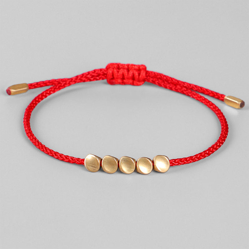 Bracelet fil rouge ajustable orné de cinq perles dorées mates disposées en ligne, sur fond gris.