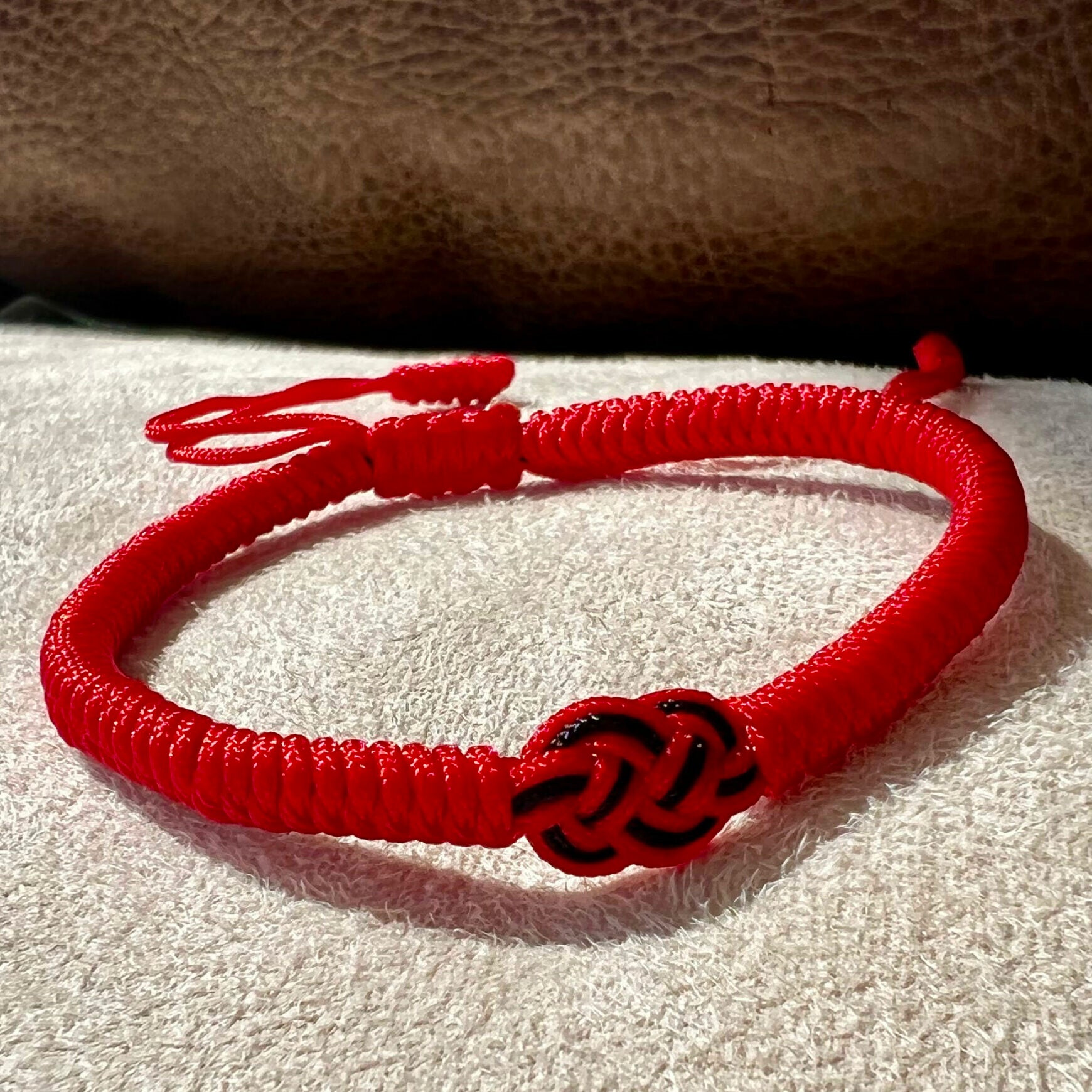 Bracelet en fil rouge tressé avec un nœud noir au centre, symbolisant la protection et la chance.