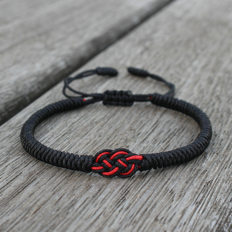 Bracelet fil rouge noir avec un nœud celtique tressé sur un fond en bois